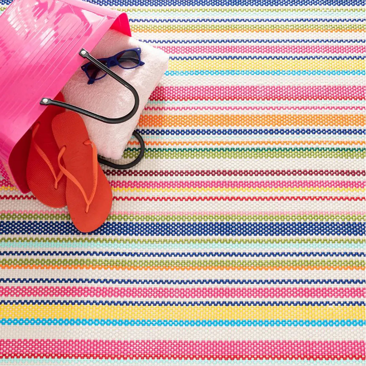 Dash and Albert Summer Stripe Handwoven Indoor Outdoor Rug with a beach bag with flip flops, towel and sunglasses on top