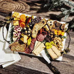 Michael Aram Small Butterfly Ginkgo Cheeseboard with Knife set outside on a wood table filled with food
