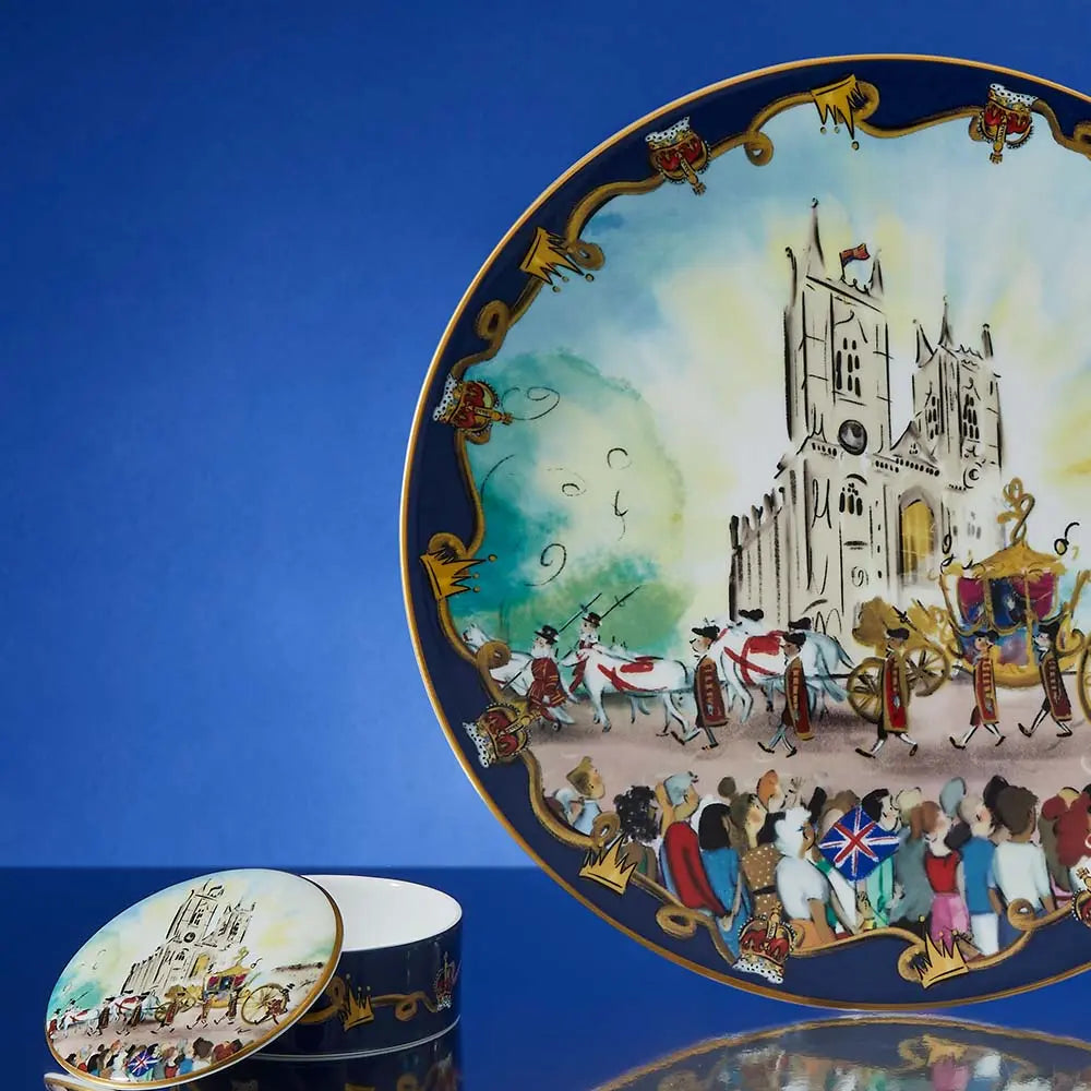 Halycon Days The Coronation at Westminster Abbey Trinket Box set in a room, lid partially off with blue background next to a large plate with the same pattern 