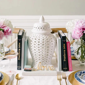 Nora Fleming BKMO Mini Occasions Book set by a white decorative vase on a dining table with other books and dinnerware