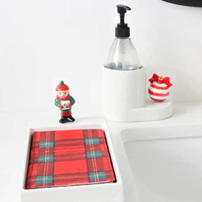 Nora Fleming Cutie Container in a white room with a red and white ornament mini and a soap bottle inside, set next to a napkin holder with plaid napkins