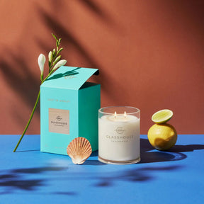 Glasshouse Fragrances Lost in Amalfi Soy Candle Sea Mist 380 grams 13.4 ounces lit and set on a table with a lemon, lime, shell and a floral stem in a room