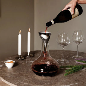 A person pouring wine through the Georg Jensen Stainless Steel Sky Wine Decanter Aerating Funnel with Filter set on a table