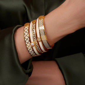 A woman wearing Halcyon Days Agama Forget-Me-Not Bangle in Cream Gold with other styles of bangles
