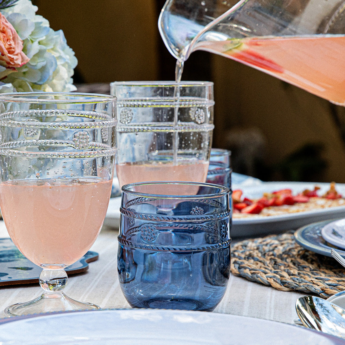 Image of clear and blue glassware cups on table setting with glass pitcher pouring pink drink.