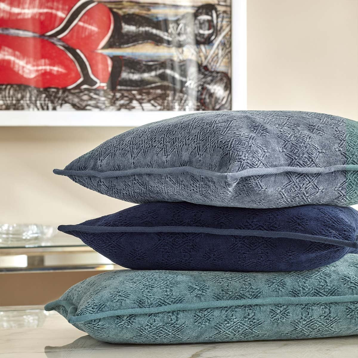 Image of stacked blue pillows on a counter with accent table and painting in background
