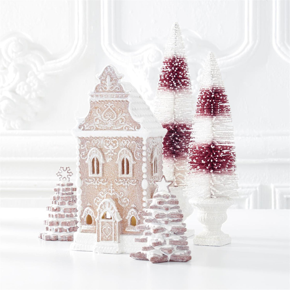 Image of white frosting covered gingerbread house on a white table and white textured wall background