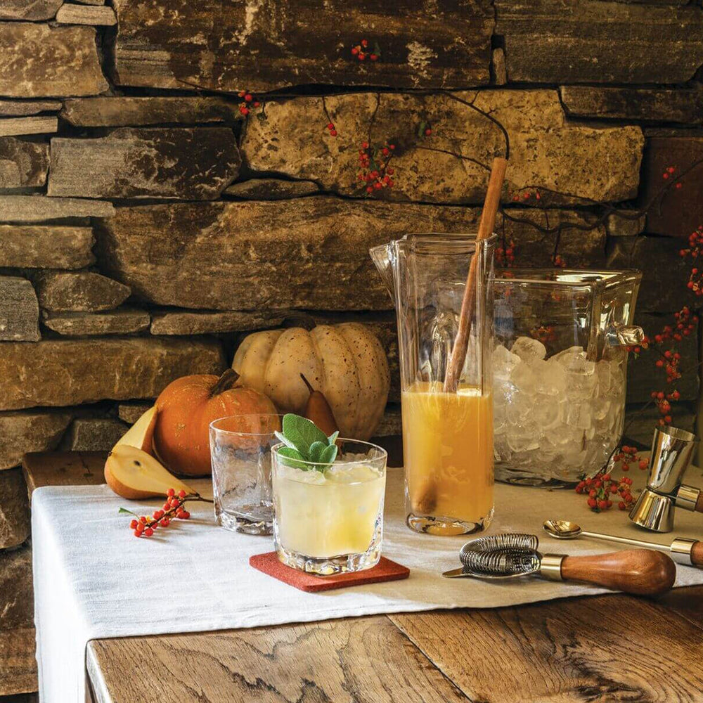 Image of glassware and bar tools on wooden table with stone wall behind