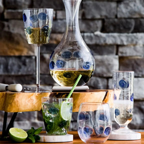 Vietri Drop Filled Wine Glass, stemless glass and champagne flute in Blue on a wood table along side a decanter and a lime