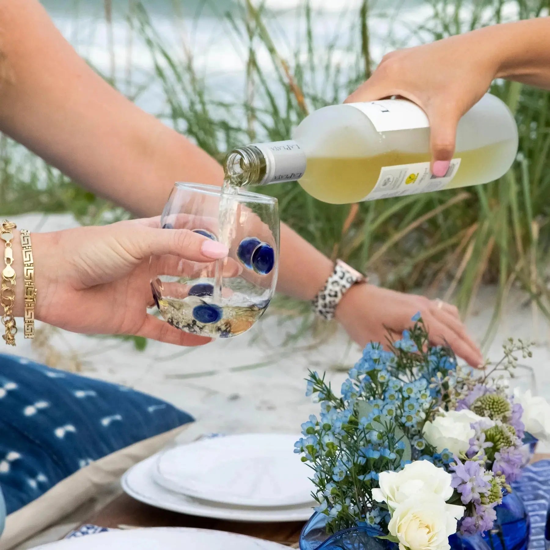 Someone pouring white wine into a Vietri Drop Blue Stemless Wine Glass in a beach setting