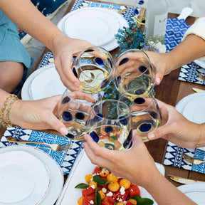Five people holding a Vietri Drop Blue Stemless Wine Glass filled with white wine over a table setting