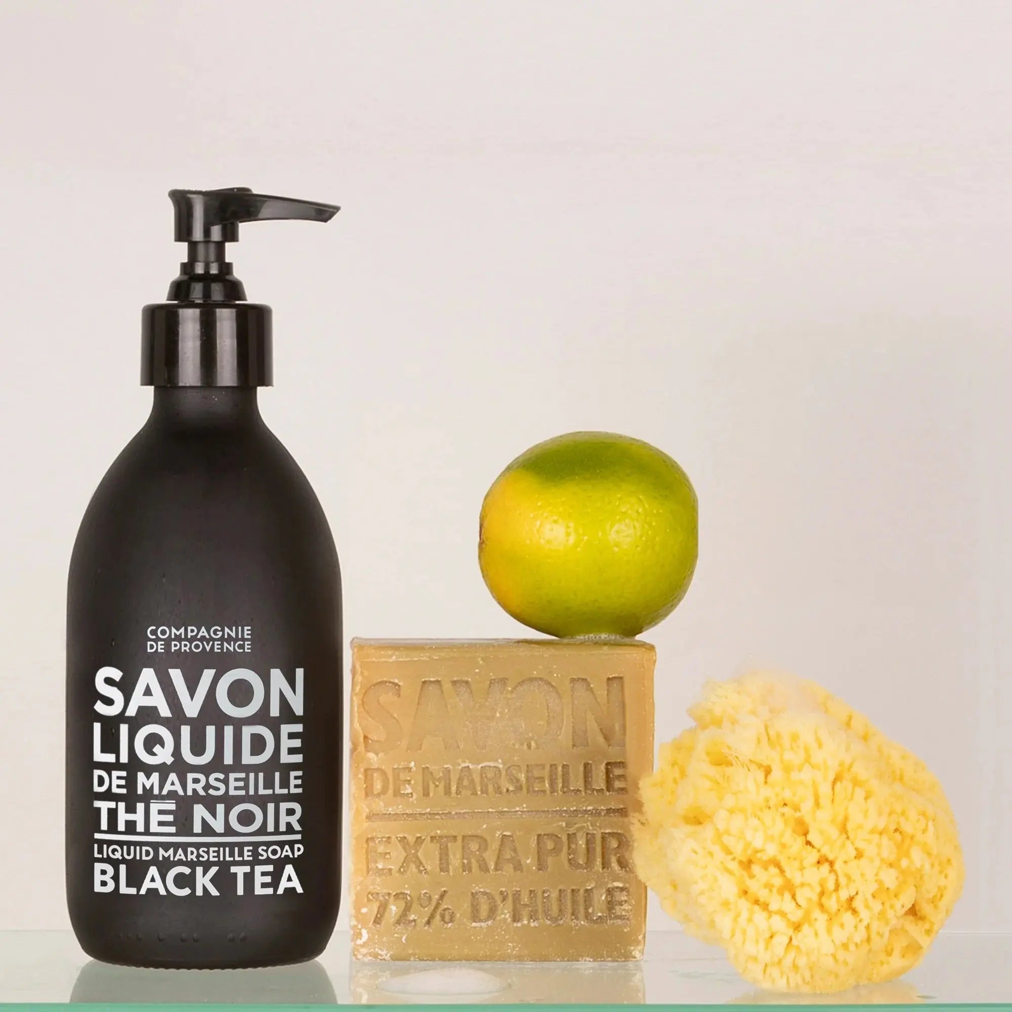 Compagnie de Provence Marseille Black Tea Liquid Soap and soap bar with a sponge and lime in a room