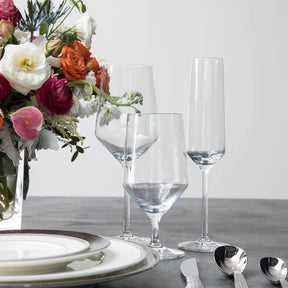 Empty Fortessa Tritan Pure Champagne Flute set on a table with other glasses and floral arrangements