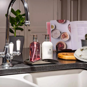 Molton Brown Rhubarb and Rose Hand Lotion set by the kitchen sink along side a cookbook and the hand soap