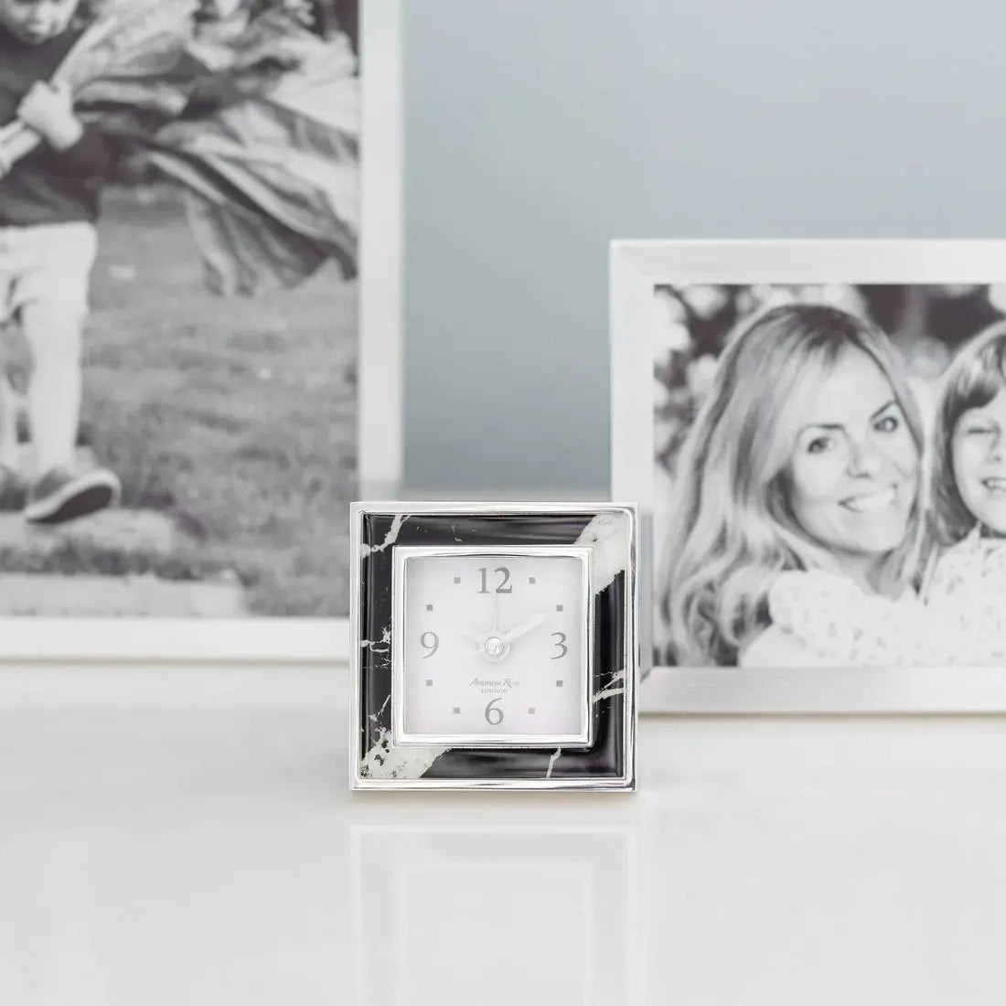 Addison Ross Black Marble Alarm Clock on a table next to other frames holding images of a lady and child 