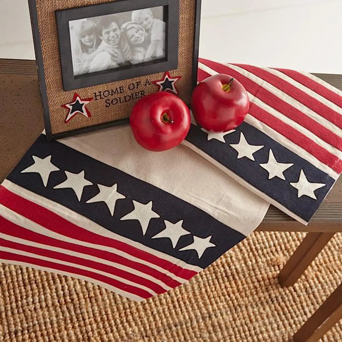 K and K Interiors Red Apple laid on top of a flag on a bench with a picture frame, showing a photo of family. The Photo frame reads Home of Soldier.