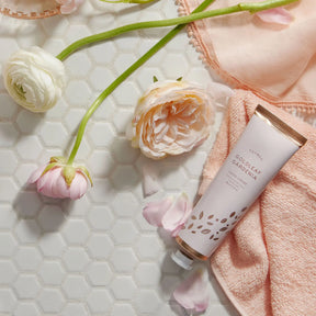 Thymes Goldleaf Gardenia Hand Cream 90 milliliter 3 fluid ounce laid on the floor next to pink flowers
