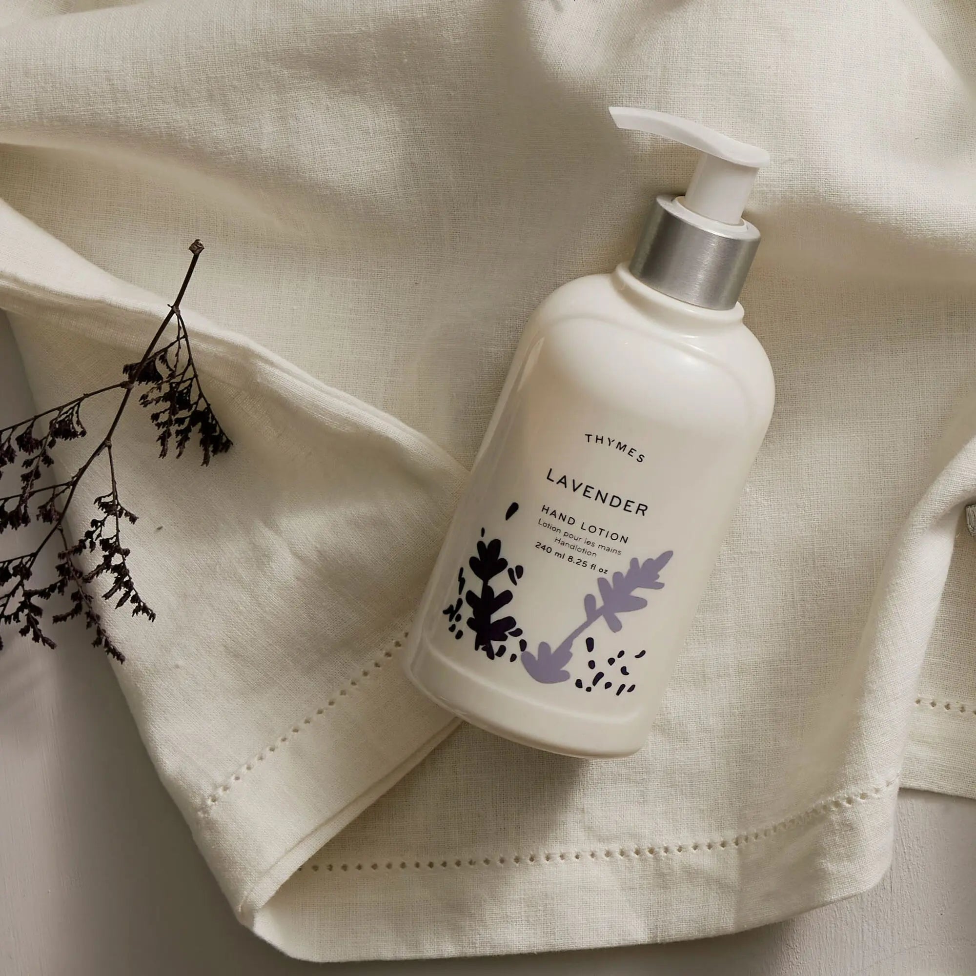 Thymes Lavender Hand Lotion 240 milliliter 8.25 fluid ounce laid on fabric with lavender
