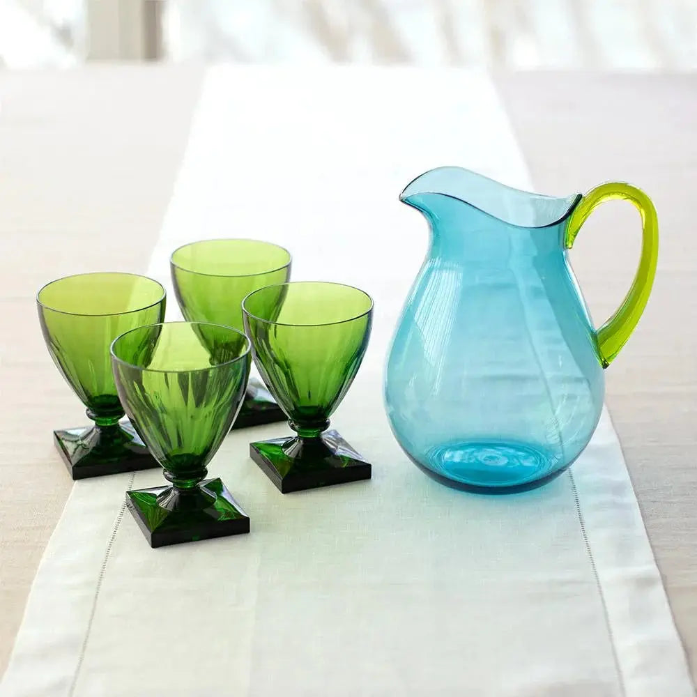 Caspari Acrylic Pitcher In Turquoise With Green Handle set on a dining room table next to four green goblets