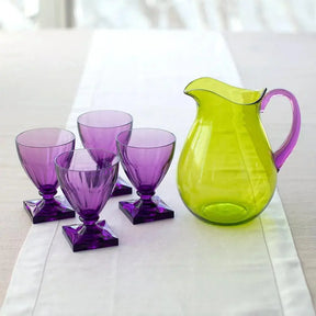 Caspari Acrylic Pitcher In Green With Amethyst Handle set on a dining room table next to four purple goblets