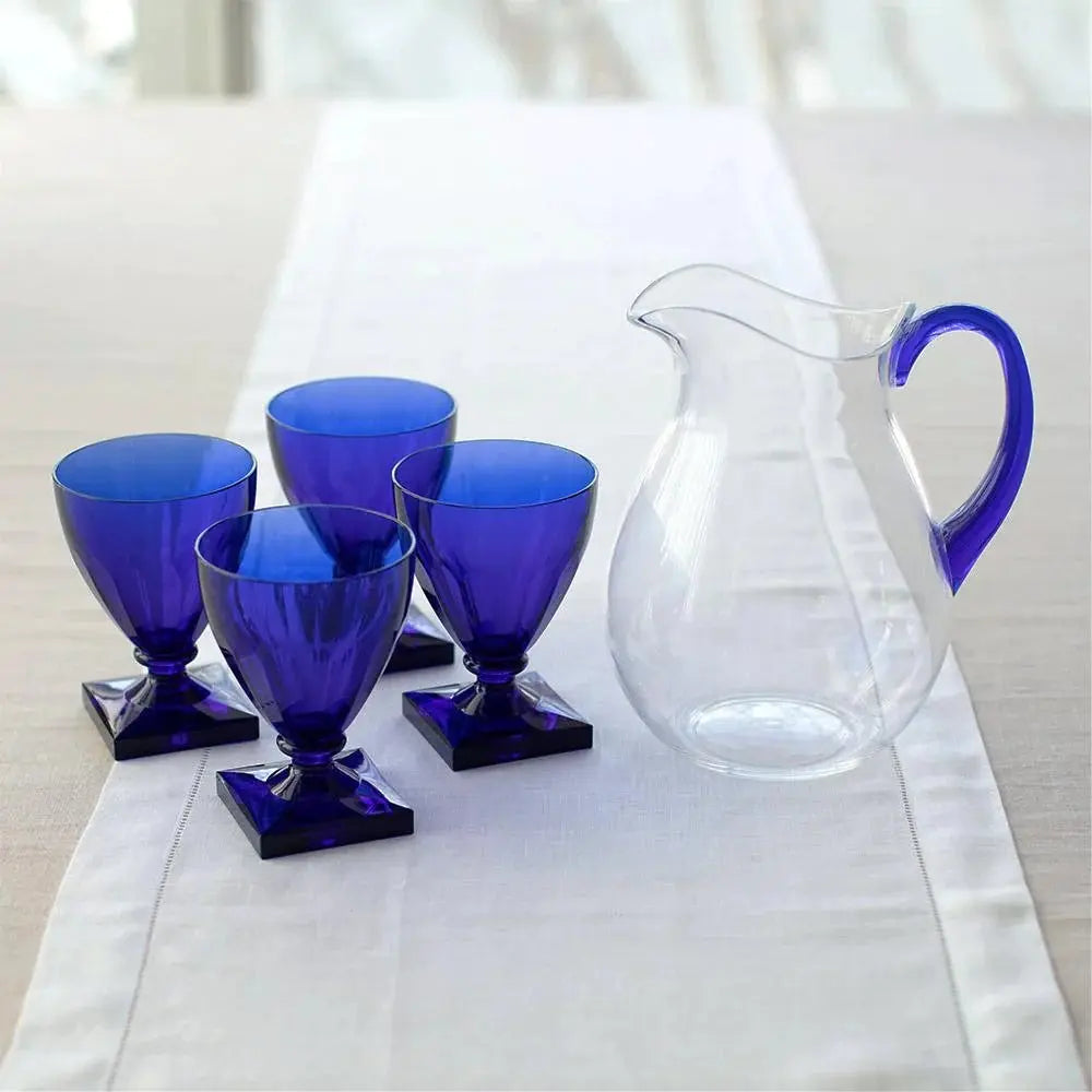Caspari Acrylic Pitcher In Clear With Cobalt Handle set on a dining room table next to four cobalt blue goblets