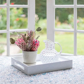 Addison Ross Lacquered Serving Tray in White on a counter with potted flowers and a glass vase in a room