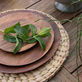 Blue Pheasant Clayton Round Placemat on a wood table with basil leaves and wood dishes.