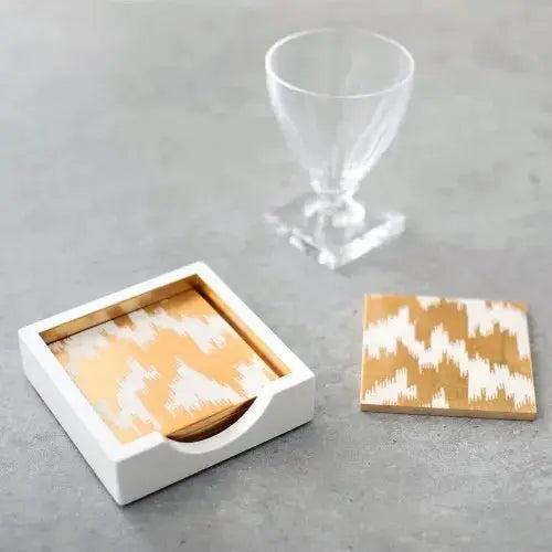 Caspari Modern Moire Coasters in Holder set on a table and next to a clear water goblet