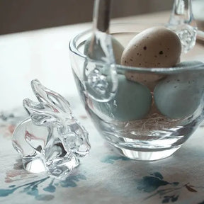 Simon Pearce Glass Rabbit set on a table next to a glass basket filled with eggs