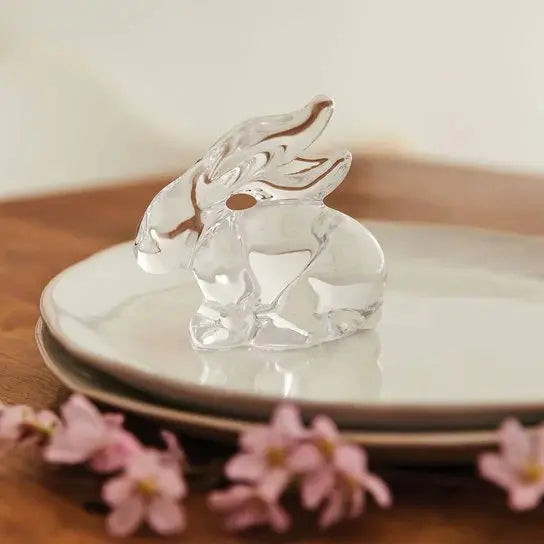 Simon Pearce Glass Rabbit set on a set of white plates with flowers in a room