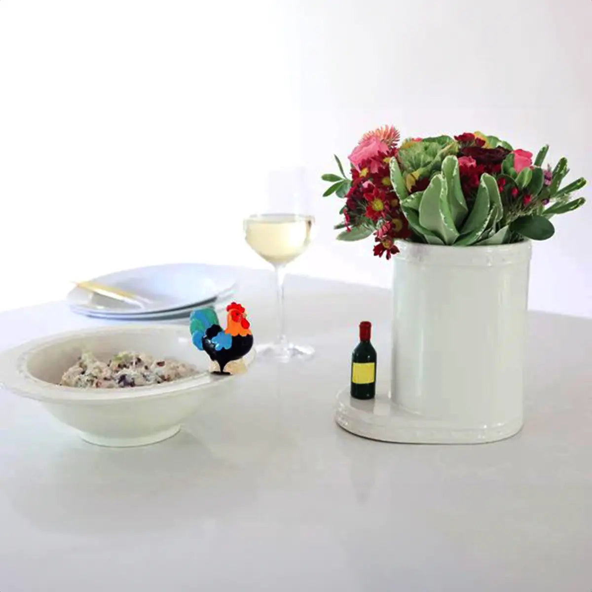 Nora Fleming Wine Bottle Mini on a flower holder with a wine glass and other accessories from Nora Fleming