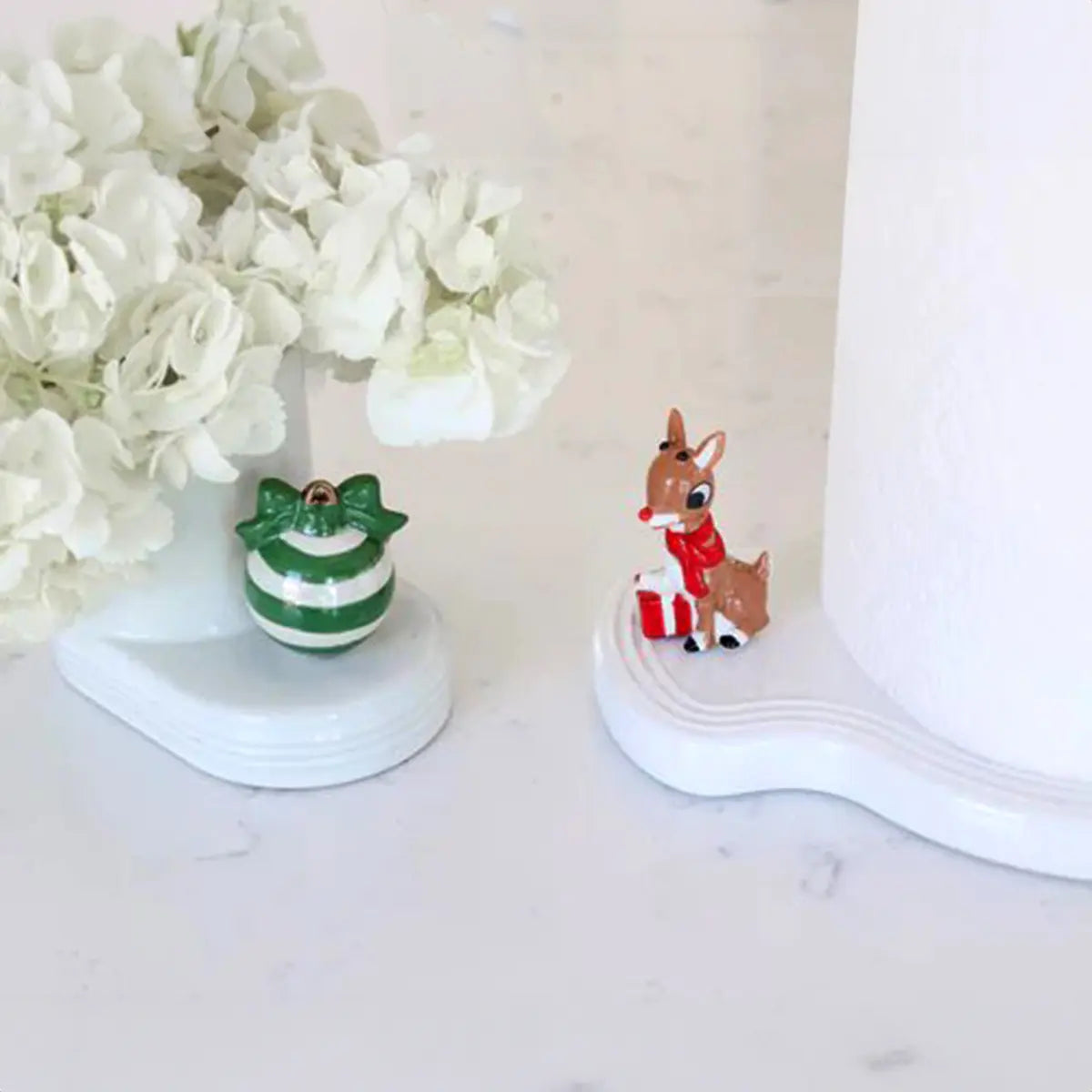 Nora Fleming Rudolph the Red-Nosed Reindeer Mini on a towel holder with flowers in a room