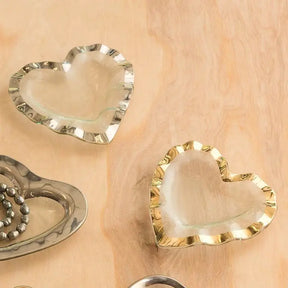 Annieglass Ruffle Heart Bowl in clear gold and clear silver laid on a table 