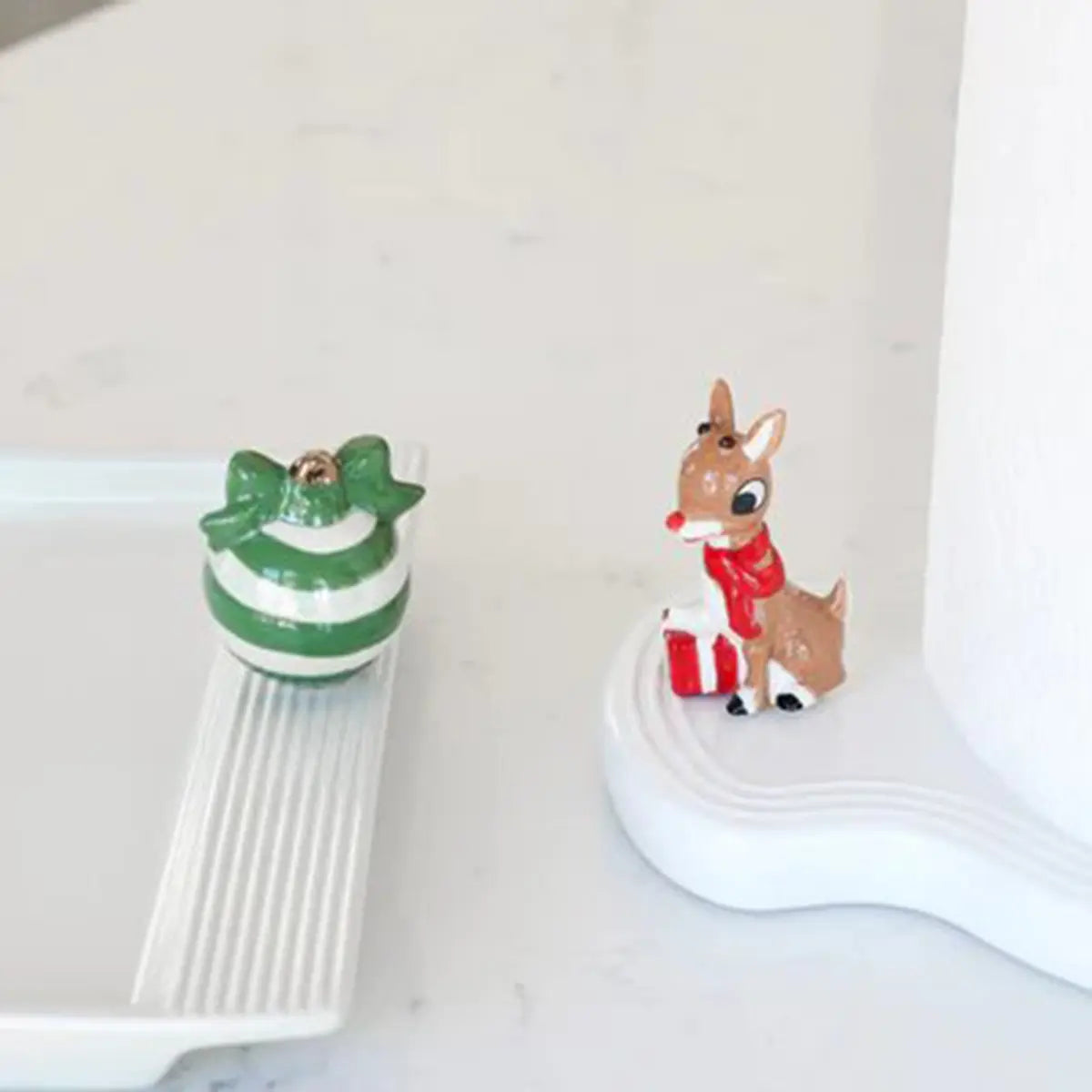 Nora Fleming Melamine Paper Towel Holder with a reindeer and present mini on a marble counter.