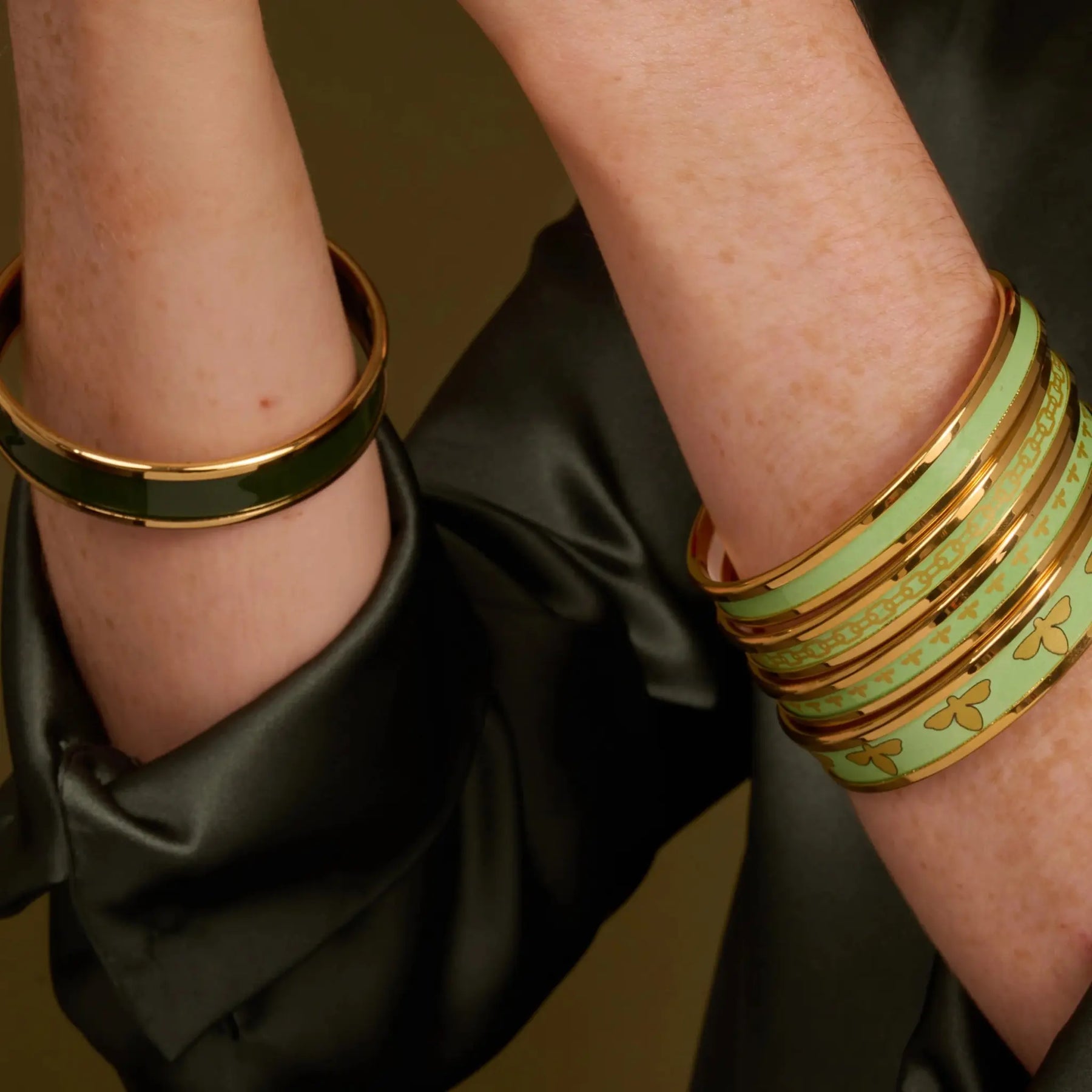 A woman wearing Halcyon Days Bee Enamel Bangle in Meadow Gold stacked with other bangles in meadow green