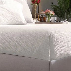 Lili Alessandra Dawn Diamond Quilted Coverlet in one hundred percent White Hemp Herringbone draped on a bed in a room