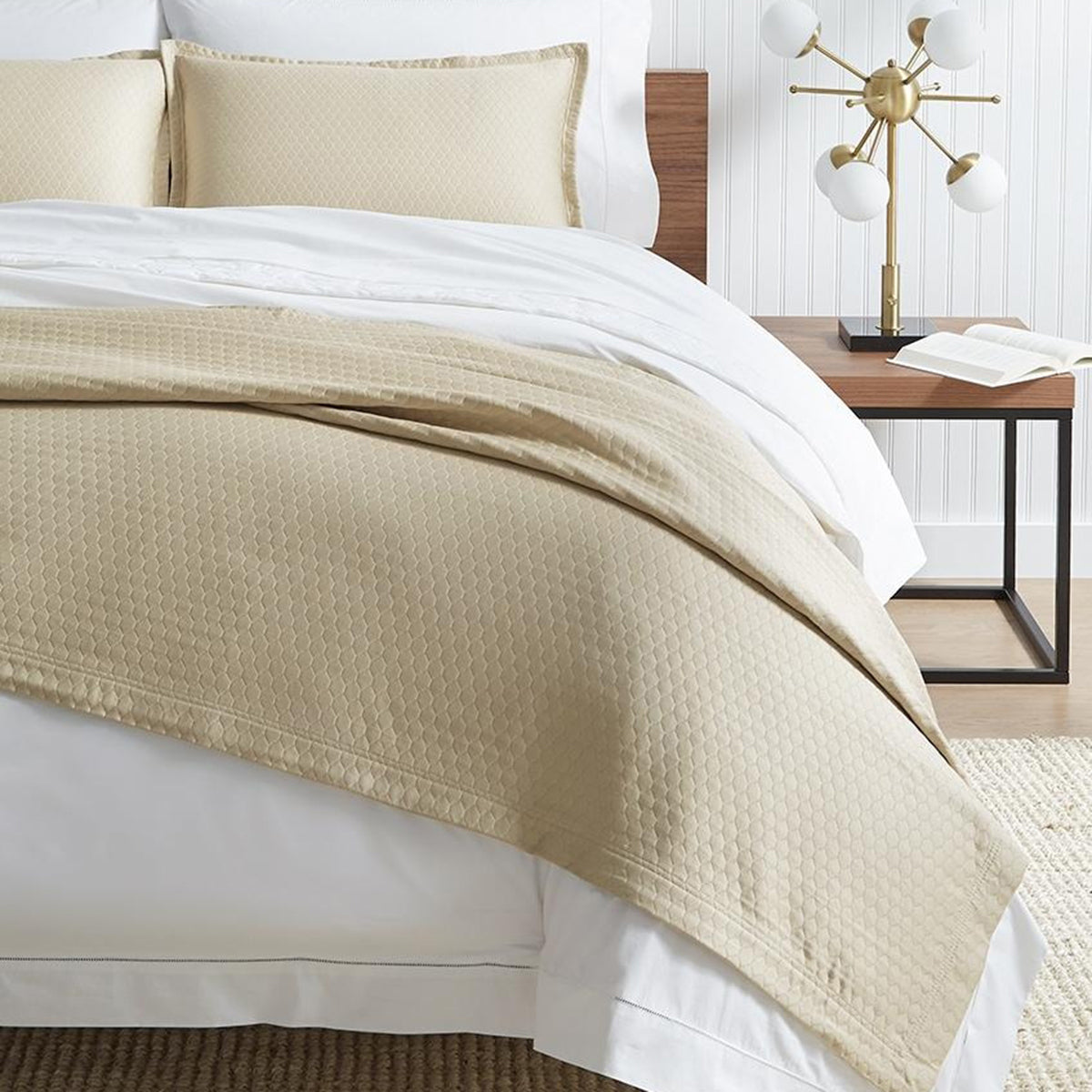 Image of a bed with a white comforter and a tan colored cover draped on top of comforter