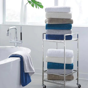 Sferra Sarma Bath Towel in various colors stacked on a rolling cart within the bathroom and also drapped on the side of a tub.