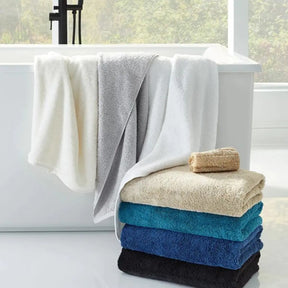 Sferra Sarma Bath Towel in various colors stacked on the floor in a bathroom and also drapped across the side of the tub.