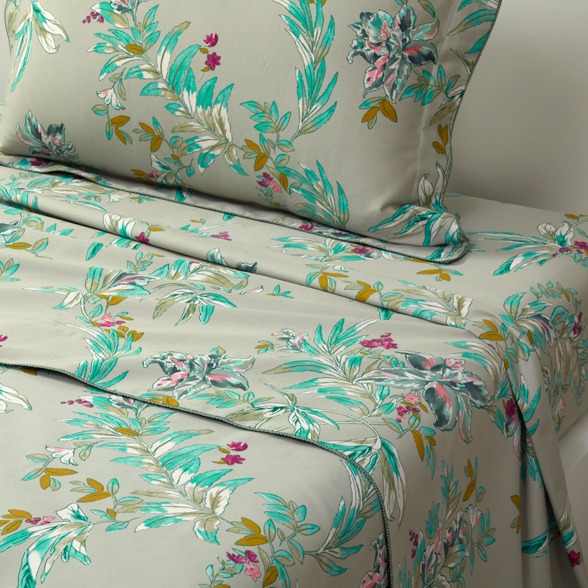 Image of a bed corner made with a dark grey green with a turquoise and white floral print set of sheets