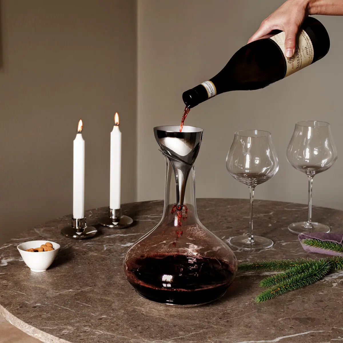 A person pouring wine through the Georg Jensen Stainless Steel Sky Wine Decanter Aerating Funnel with Filter set on a table