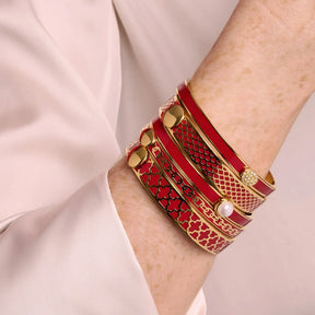 A woman wearing Halcyon Days Agama Forget Me Not Bangle in Red Gold with other red bandles.